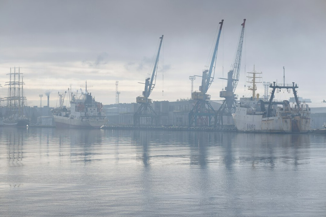 Foggy harbor at dusk with old cranes and moored boats